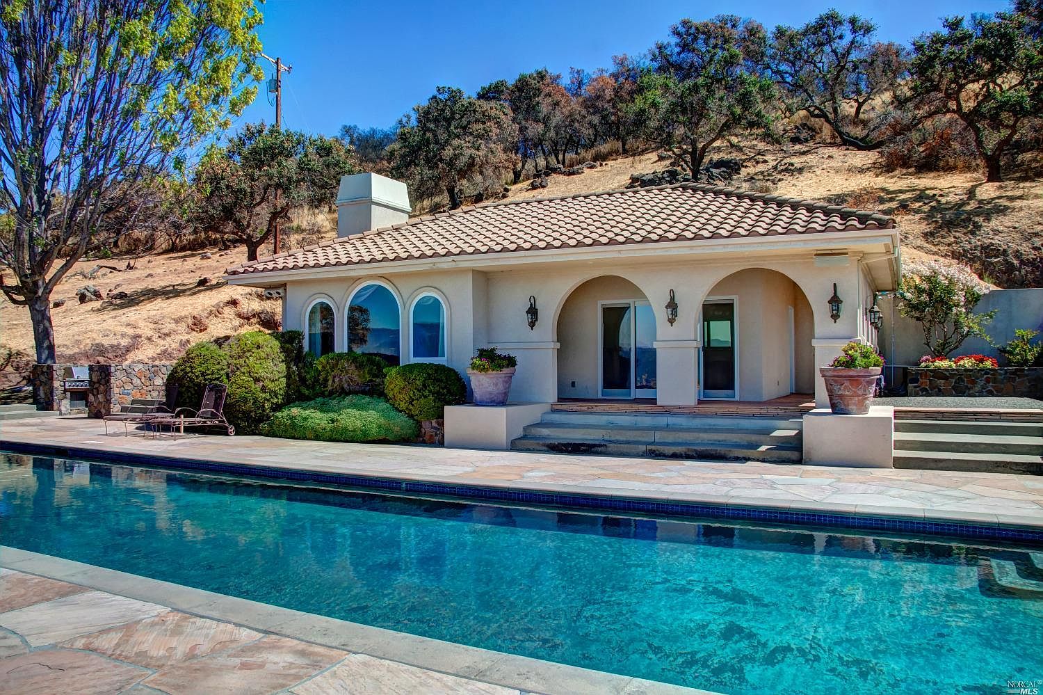 The Mediterranean pool pavilion in stucco and tile, framed by oak hillsides above the lap pool.