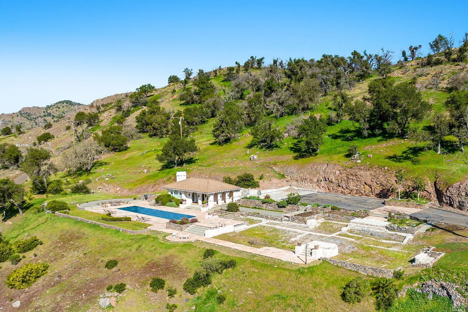 Aerial view of the property's pool pavilion and existing improvements set into the hillside, surrounded by oak woodland.