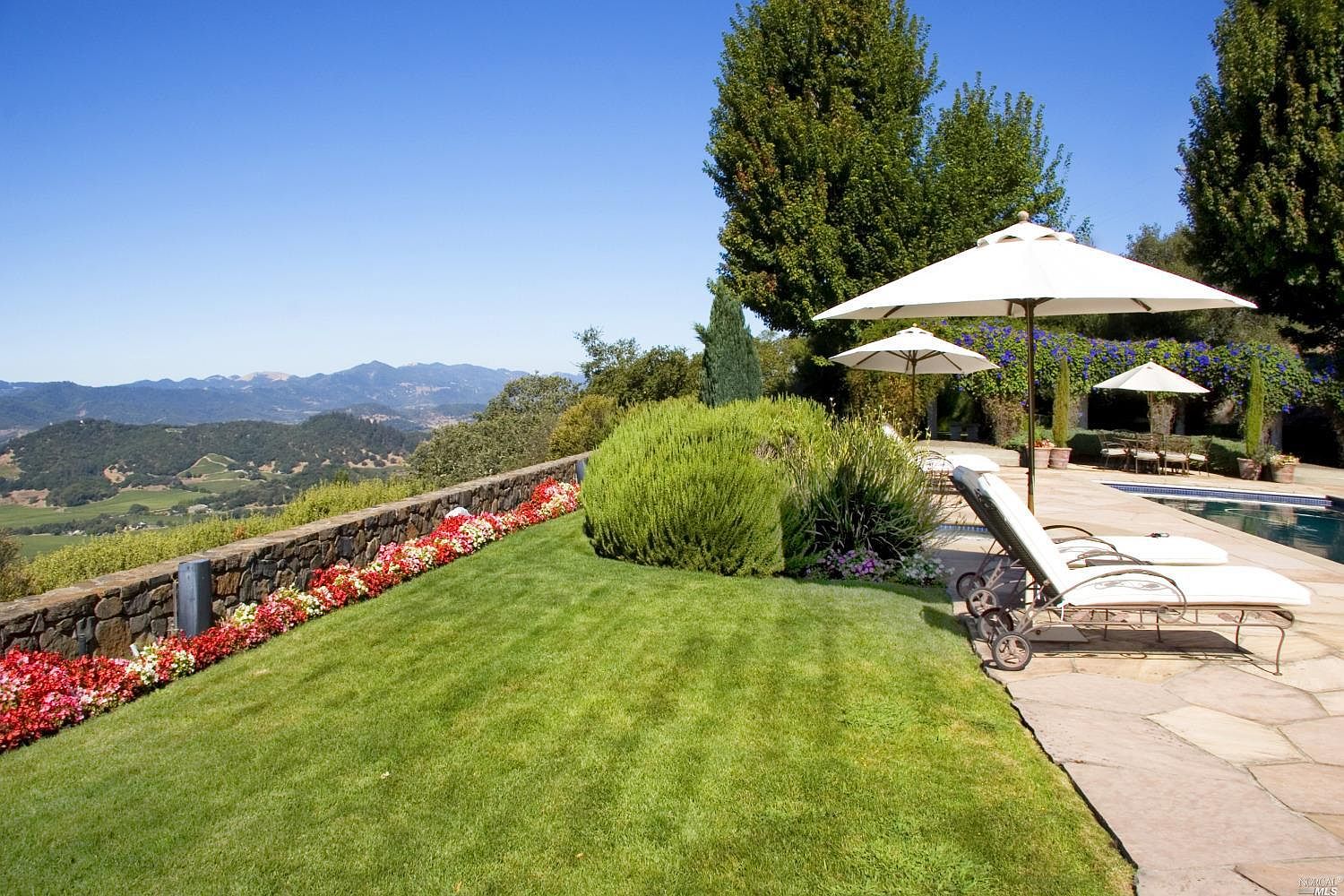 Manicured lawn and flower border running along a low stone wall, with the Mayacamas Mountains in the distance.