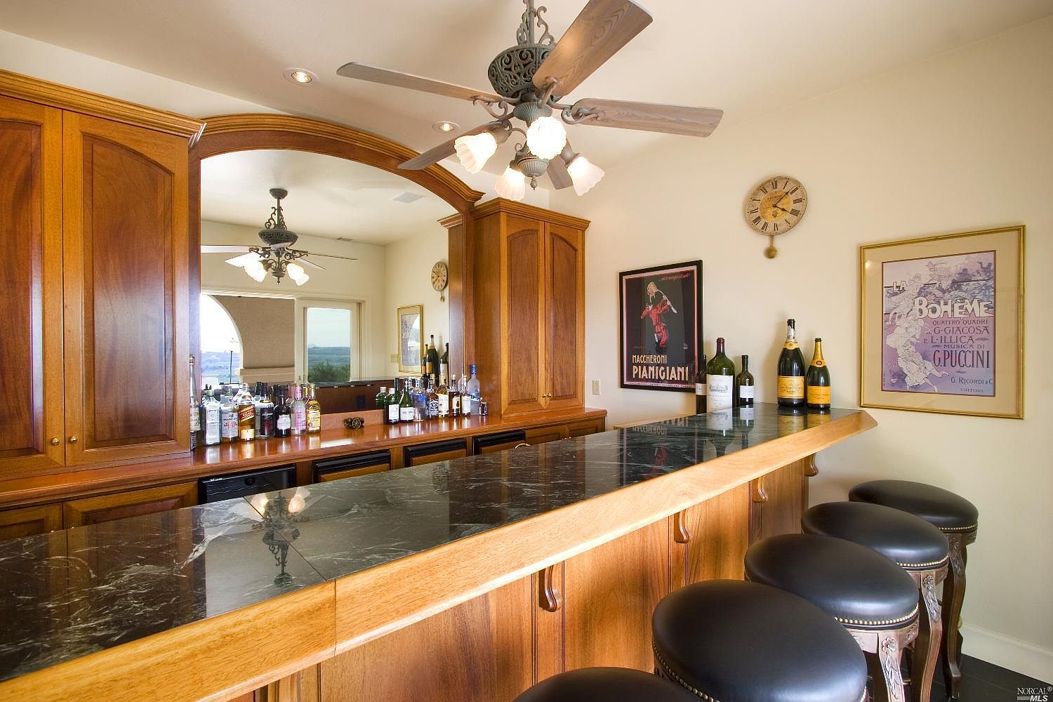 The pool pavilion's mahogany wet bar with marble counter, leather stools, and a view through arched windows to the valley.