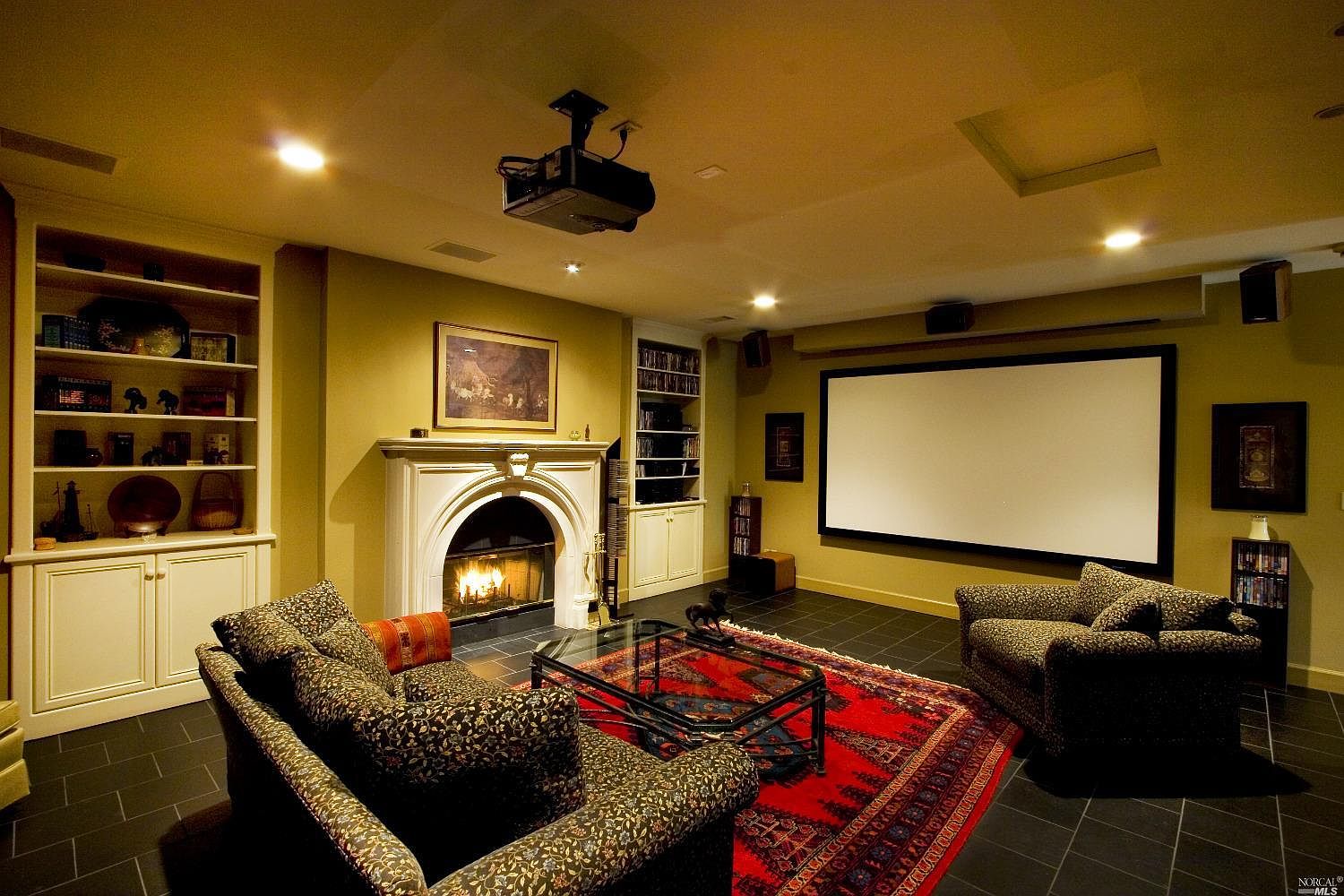A media room inside the pavilion with a stone fireplace, projection screen, and warm lighting.